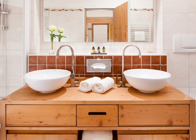 Blick in das Badezimmer einer Almenrausch Suite mit zwei Waschbecken und Holzmöbel