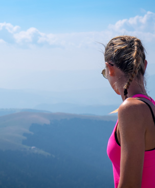 Junge Dame in Sportkleidung blick bei strahlendem Sonnenschein von Berggipfel auf das Tal