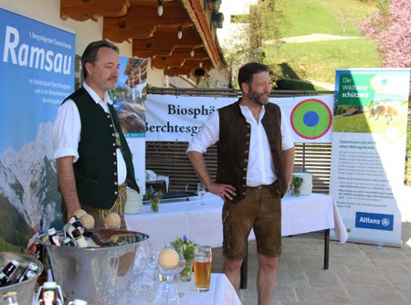 Zwei in Tracht gekleidete Männer stehen freundlich vor einem Stand zum Thema Biosphärengebiet Berchtesgaden