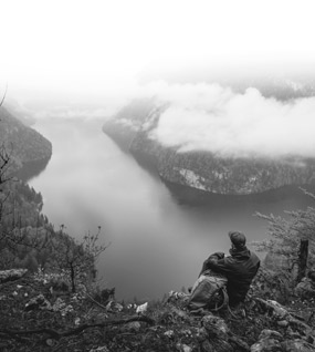 Wanderer blickt von Berggifel auf wolkenverdeckten Königssee