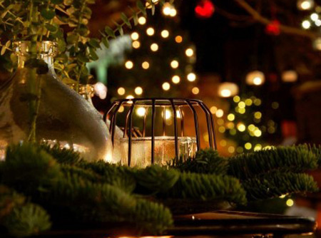 Weihnachtlich mit Tannenzweigen, Windlicht und Lichterketten dekorierter Tsich
