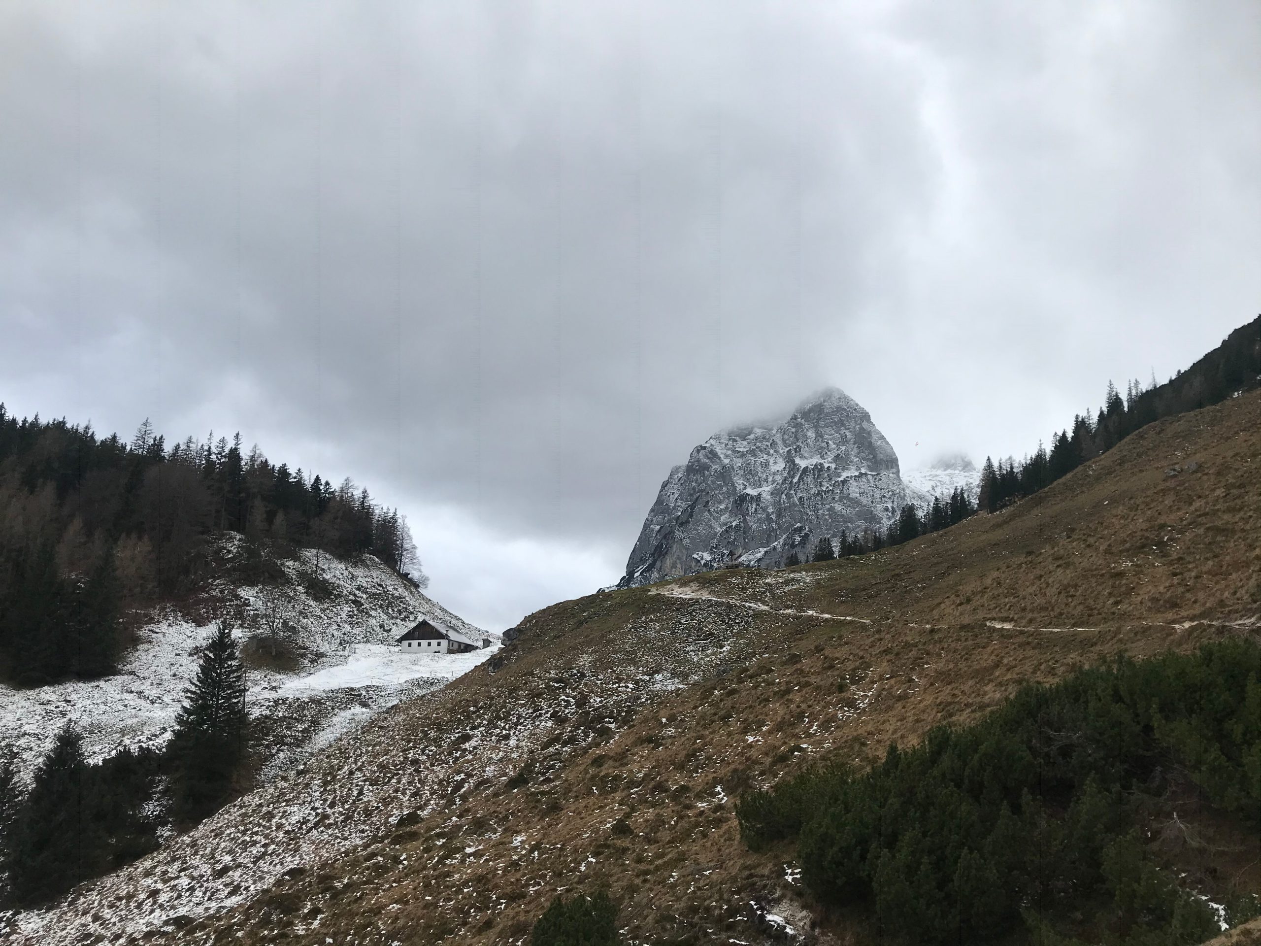 Naturaufnahme eines Wanderweges bei bewölktem Himmel und mit schneebedeckten Hängen