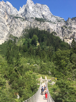 Beim Wandern im Berchtesgadener Land überqueren einige Wanderer eine Hängebrücke bei strahlendem Sonnenschein