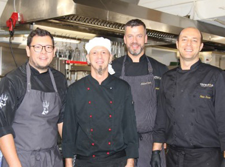 Vier in schwarzer Uniform gekleidete Köche posieren in der Küche für ein Foto